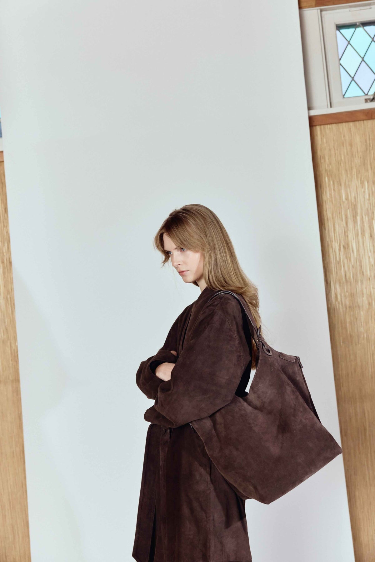 Woman wearing a brown coat with a large bag against a light-colored wall